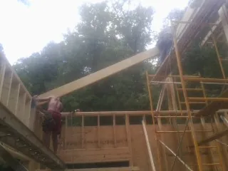 Carpenter raising a rafter beam on a new second story frame in Intercession City