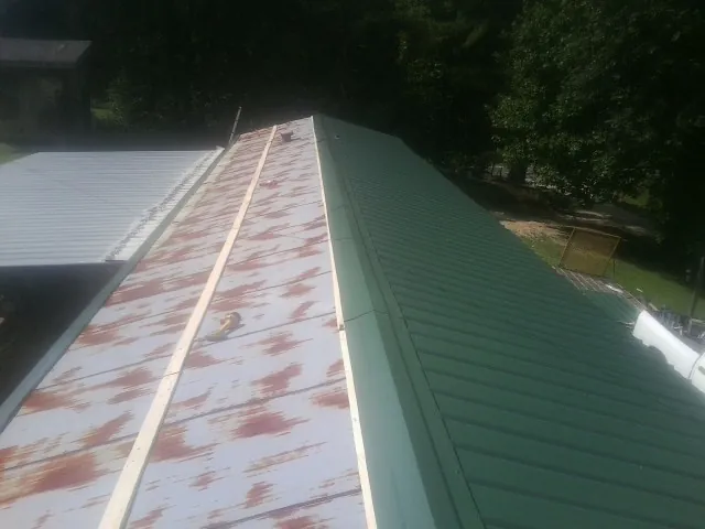 Old rusted panels beside newly installed green metal roofing — Wind Damage Roof Repair by Roofing Brothers in Intercession City